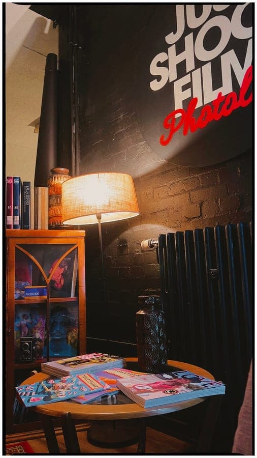 A corner of the lab with a lamp, books and the Just Shoot Film wall